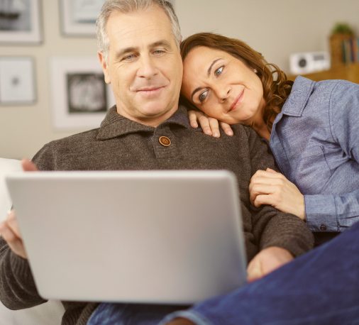 Couple relaxing on couch while looking at laptop