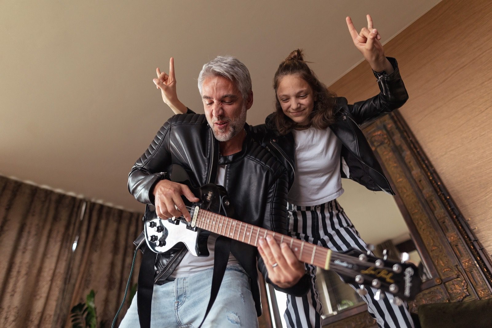 Father rock guitarist having fun and and dancing with his teenage daughter at home.