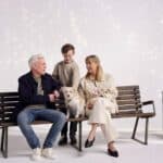 Middle aged couple and dog sitting on bench with a young boy standing and petting the dog.