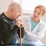 Man with a walking stick being helped by a nurse