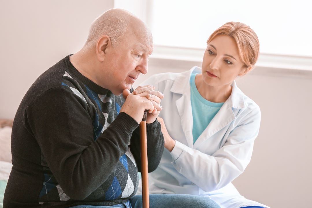 Man with a walking stick being helped by a nurse